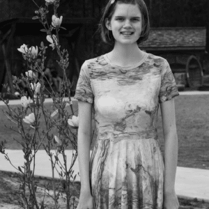 Black and white photo of a young adult woman standing outside near flowers