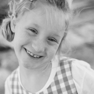 Black and white photo of child smiling with a bow in her hair outside
