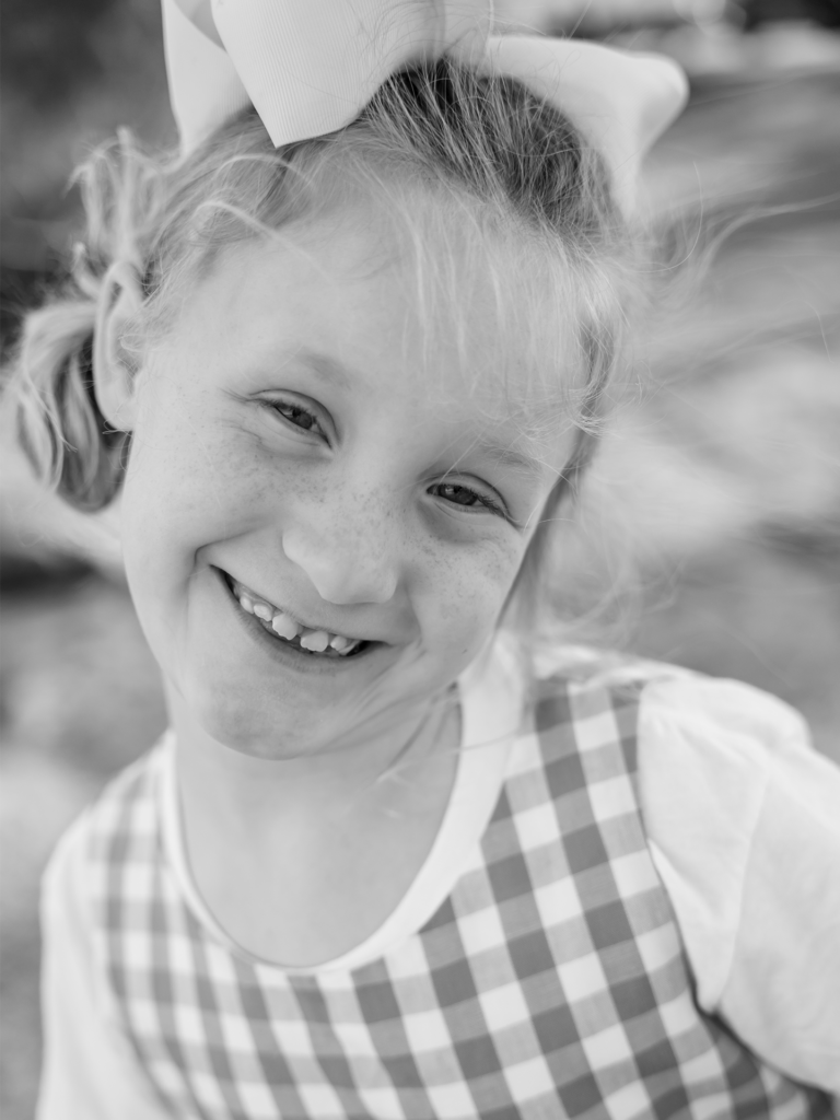 Black and white photo of child smiling with a bow in her hair outside