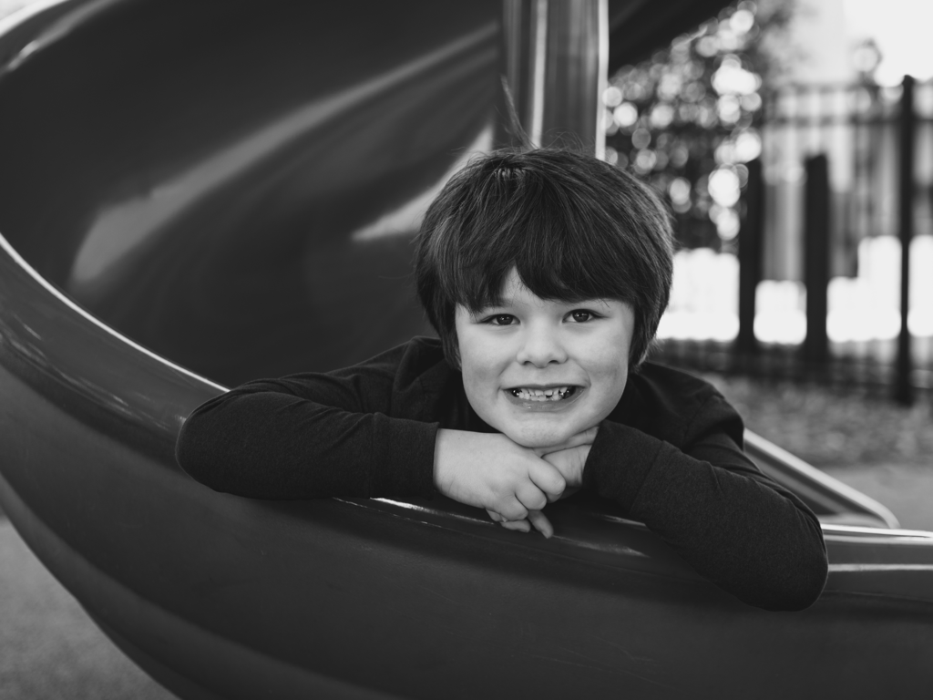 Black and white photo of child boy leaning against a slide