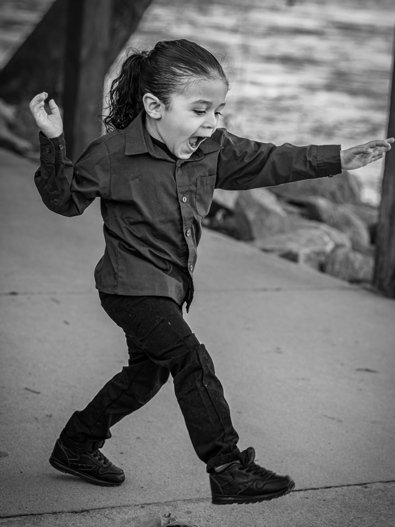 Black and white photo of toddler boy running on a sidewalk