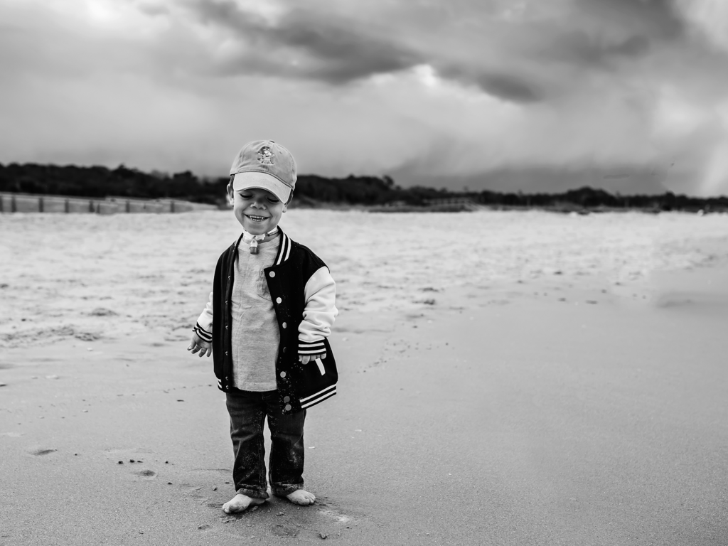 Black and white photo of toddler boy walking on the beach