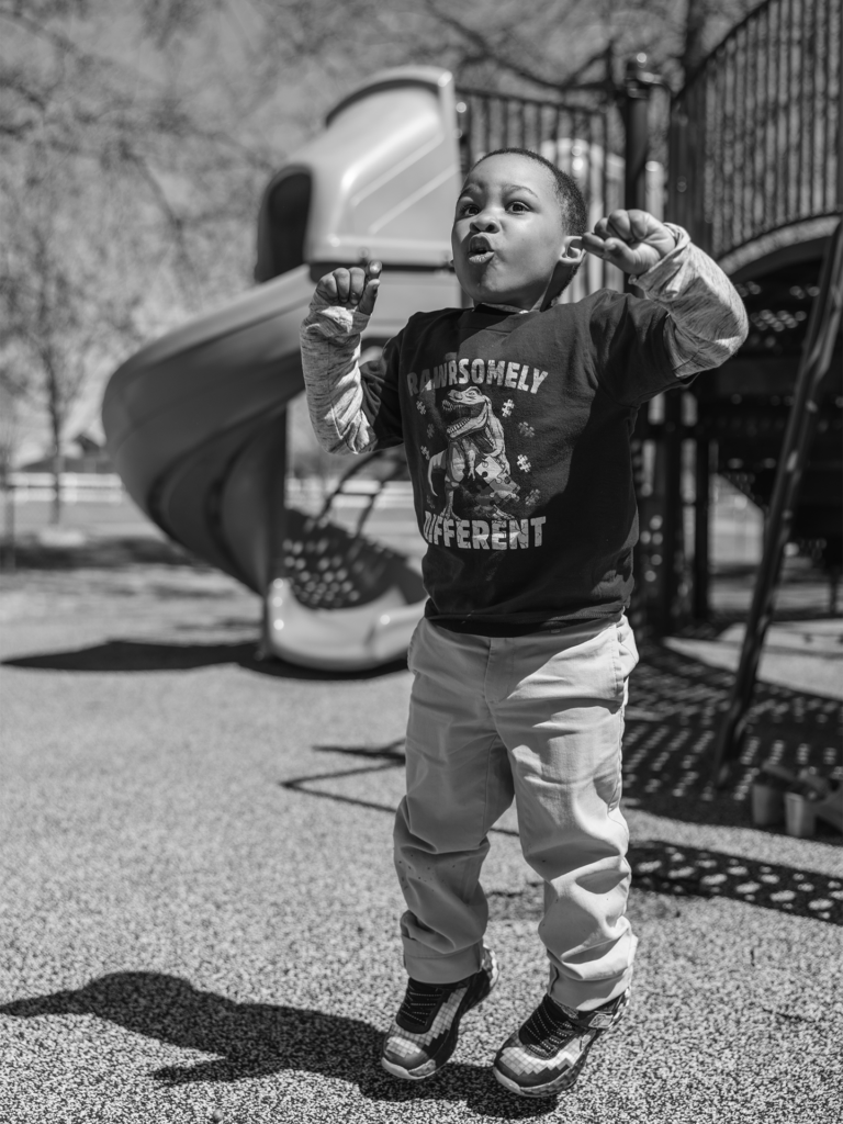 Black and white photo of toddler boy jumping at the park