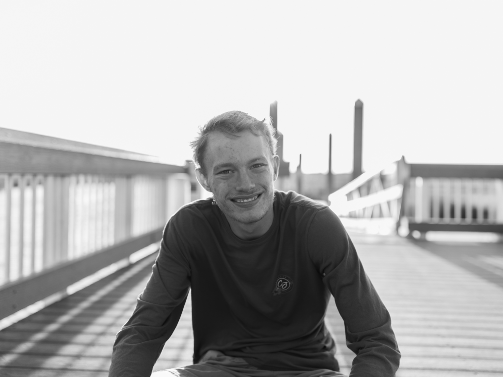 Black and white photo of a teenage male sitting on a bridge and smiling