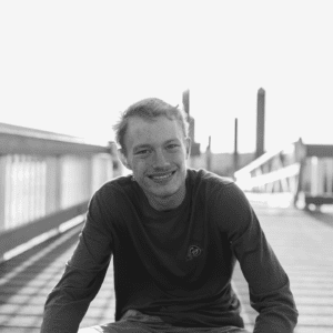 Black and white photo of a teenage male sitting on a bridge and smiling