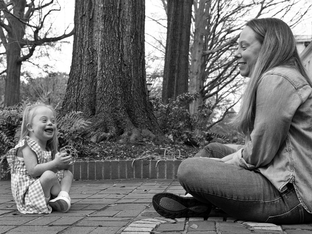 Black and white photo of toddler girl sitting across from her parent and laughing