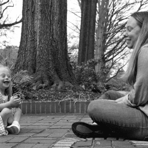 Black and white photo of toddler girl sitting across from her parent and laughing