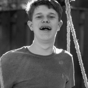 Black and white photo of a young adult male sitting on a rope swing