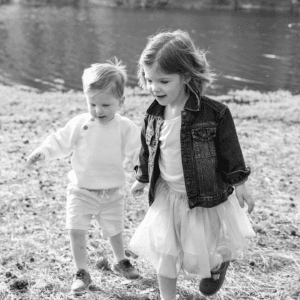 Black and white photo of a toddler aged boy and girl walking near a lake