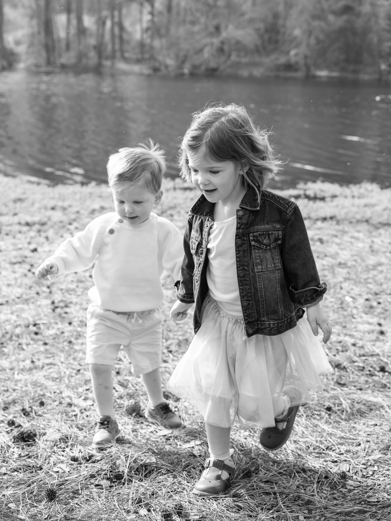 Black and white photo of a toddler aged boy and girl walking near a lake