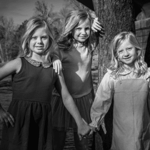 Black and white photo of three female children; two holding hands and one leaning against a tree