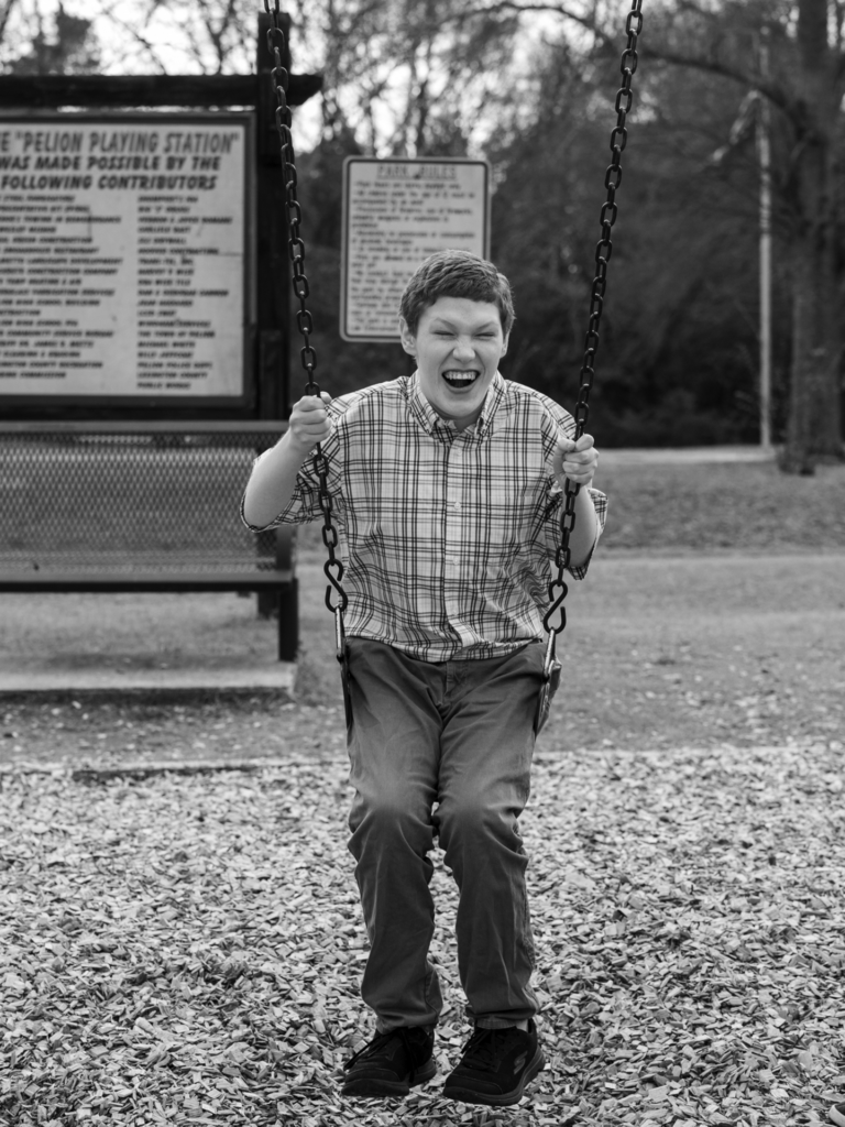 Black and white photo of young adult male on a swing in front of a large sign
