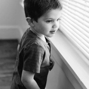 Black and white photo of a male toddler looking out of a windo