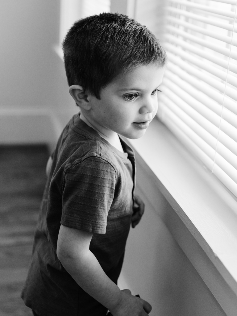 Black and white photo of a male toddler looking out of a windo