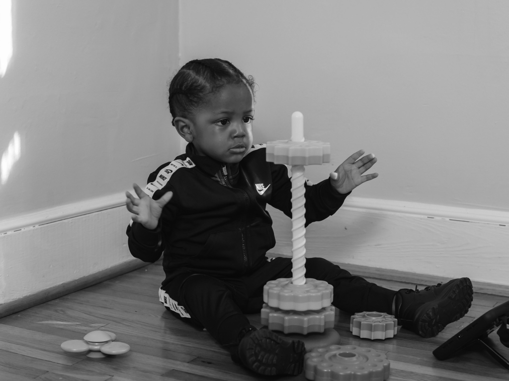 Black and white photo of a toddler playing with toy on the floor
