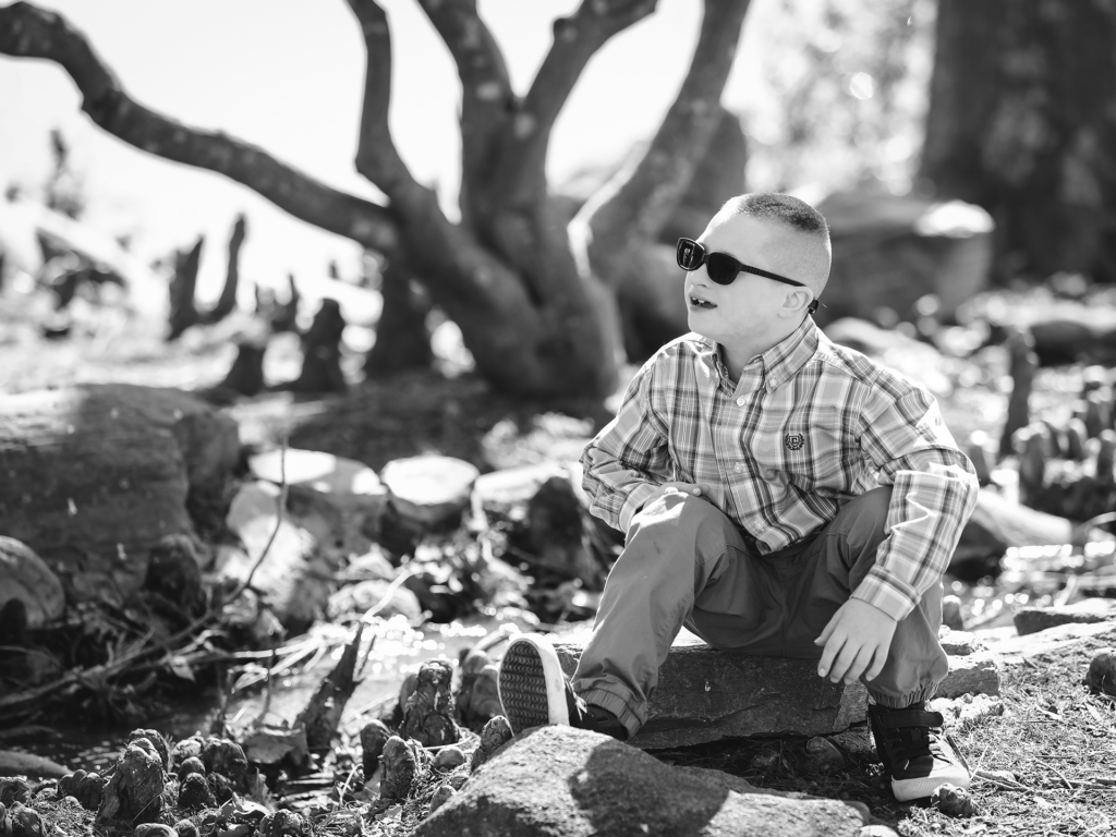 Black and white photo of male child sitting on a rock outside with sunglasses
