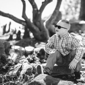 Black and white photo of male child sitting on a rock outside with sunglasses