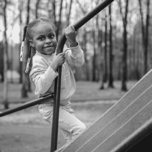 Black and white photo of female child holding onto playground equipment and smiling