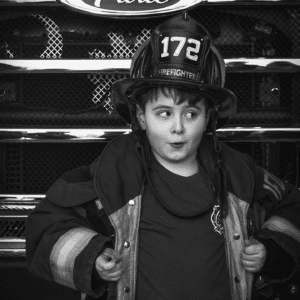 Black and white photo of male child in fireman uniform looking to the side