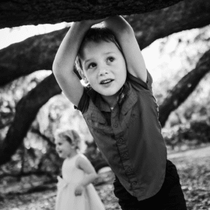 Black and white photo of male child leaning against tree with looking away