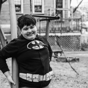 Black and white photo of male child in batman jacket smiling in his backyard