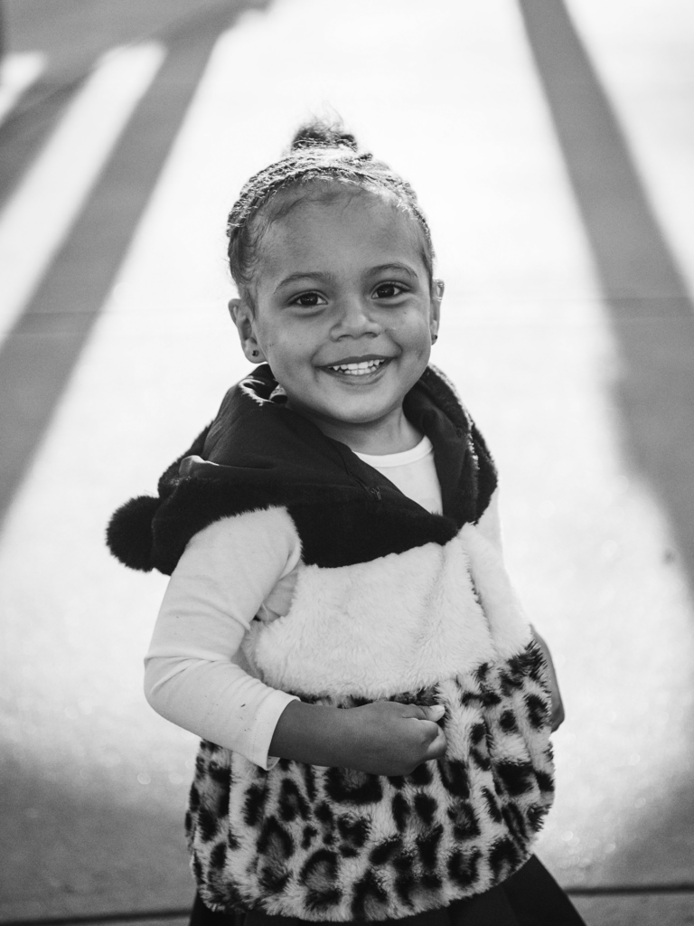 Black and white photo of toddler female smiling outside in a furry vest and skirt