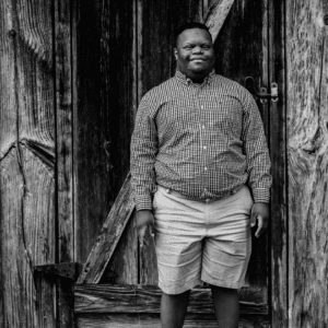 Black and white photo of young adult standing in front of wooden door and smiling