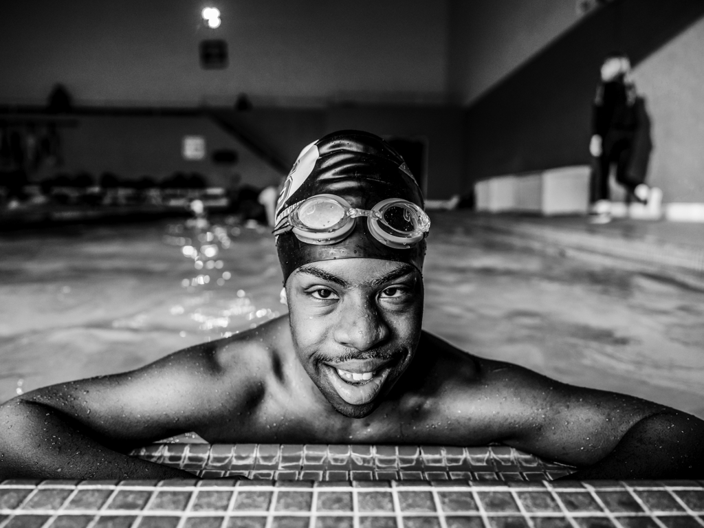 Black and white photo of young adult male swimming in a pool with goggles