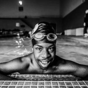 Black and white photo of young adult male swimming in a pool with goggles