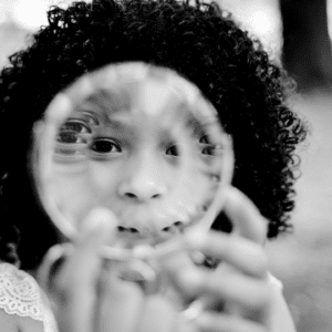 Black and white photo of female child looking through spiral ring