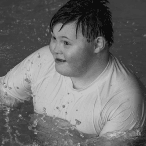 Black and white photo of young adult male swimming in a white shirt
