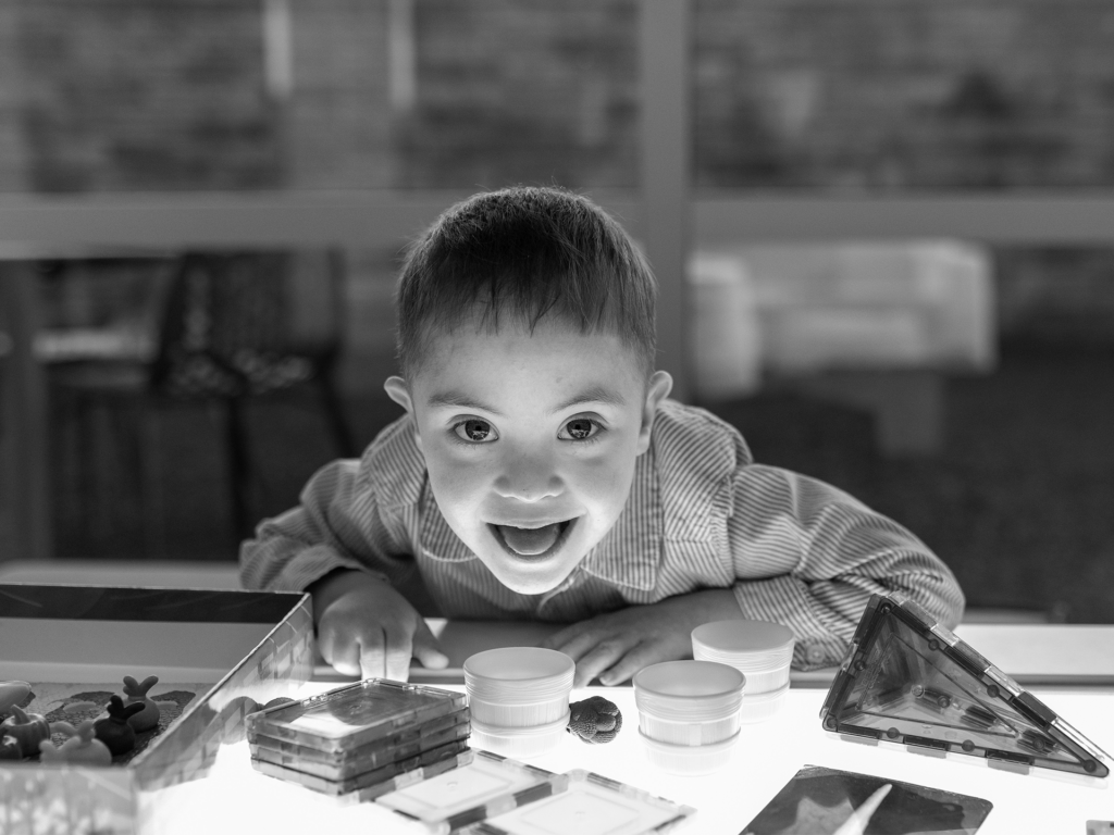 Black and white photo of male toddler leaning against table with toys