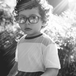 Black and white photo of toddler male with glasses standing in sunlight