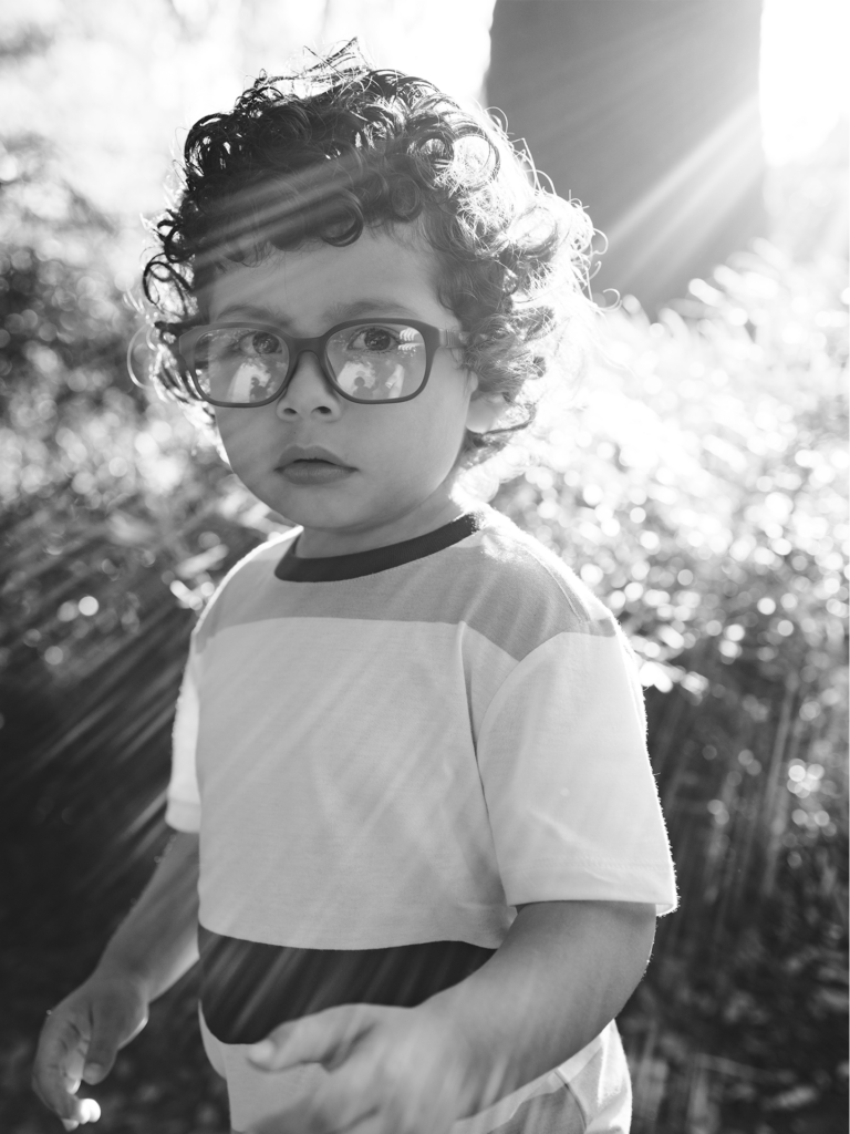 Black and white photo of toddler male with glasses standing in sunlight