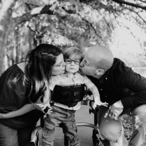 Black and white photo of male toddler being kissed my parents on each cheek