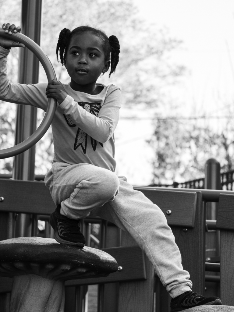 Black and white photo of female child sitting on playground equipment looking away